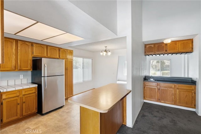 kitchen featuring tile countertops, light carpet, hanging light fixtures, stainless steel refrigerator, and kitchen peninsula