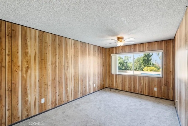 spare room featuring wooden walls, light colored carpet, a textured ceiling, and ceiling fan