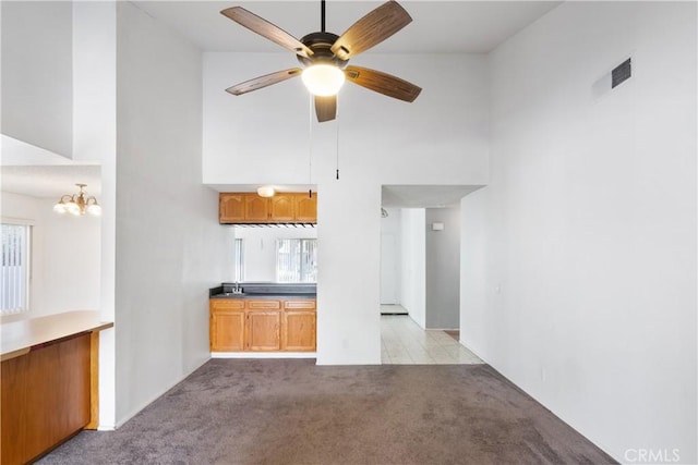 unfurnished living room featuring light carpet, ceiling fan with notable chandelier, plenty of natural light, and a high ceiling