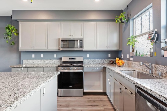 kitchen with sink, light wood-type flooring, stainless steel appliances, and light stone countertops