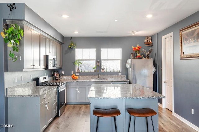 kitchen with light hardwood / wood-style flooring, appliances with stainless steel finishes, a kitchen island, light stone countertops, and a kitchen bar