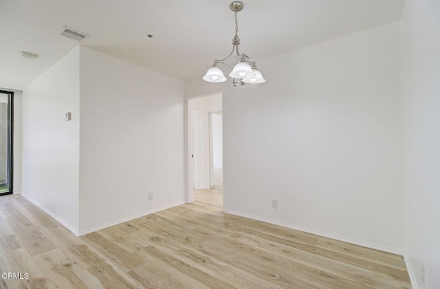 empty room featuring a notable chandelier and light wood-type flooring