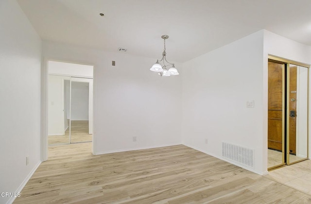 spare room featuring a chandelier and light wood-type flooring