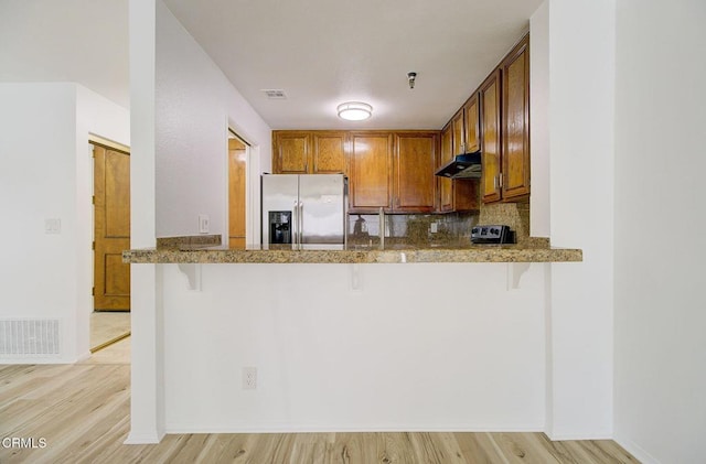 kitchen featuring backsplash, a kitchen breakfast bar, light hardwood / wood-style floors, kitchen peninsula, and stainless steel refrigerator with ice dispenser