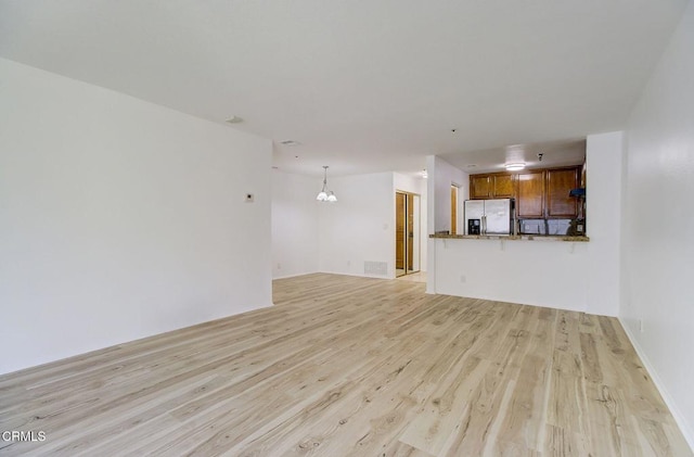 unfurnished living room featuring a notable chandelier and light wood-type flooring