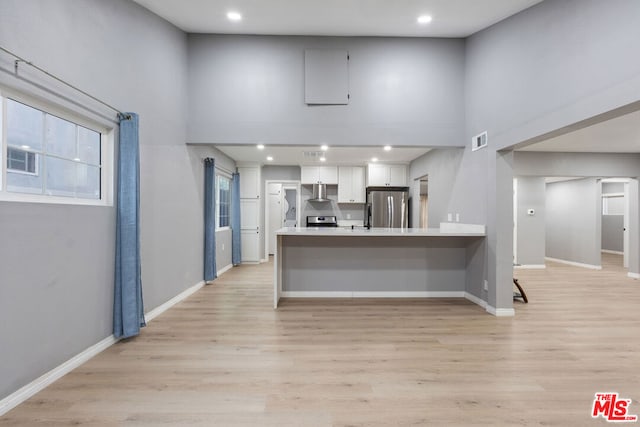 kitchen with stainless steel appliances, a towering ceiling, white cabinets, and kitchen peninsula