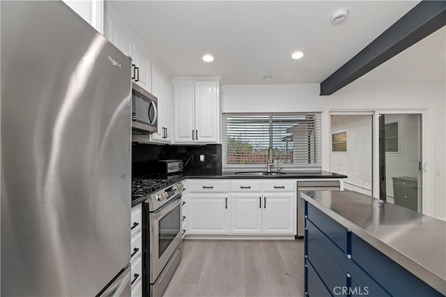 kitchen with sink, blue cabinetry, backsplash, stainless steel appliances, and white cabinets