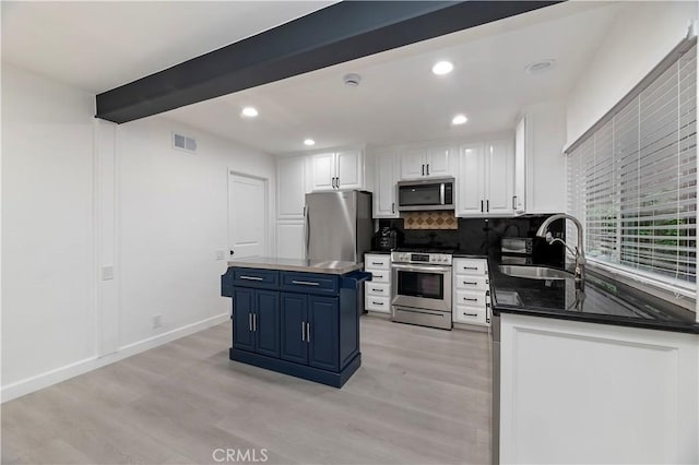 kitchen with appliances with stainless steel finishes, beamed ceiling, blue cabinets, sink, and a center island