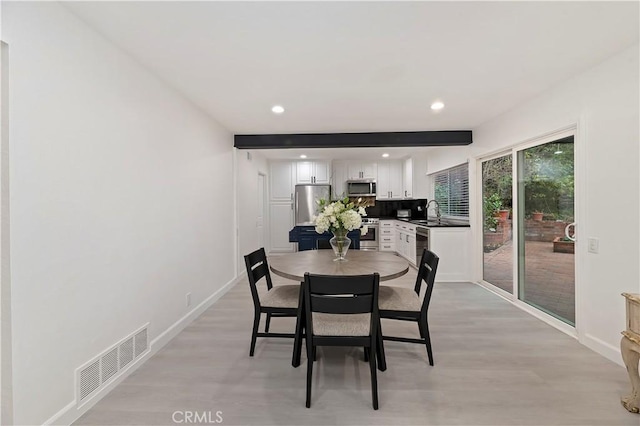 dining space featuring beamed ceiling, sink, and light wood-type flooring