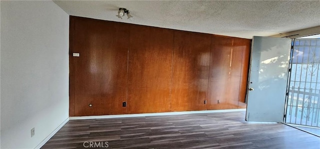 spare room with dark hardwood / wood-style floors, a textured ceiling, and wood walls