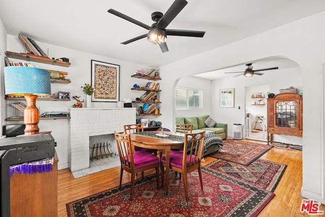 dining room with hardwood / wood-style flooring, ceiling fan, and a fireplace