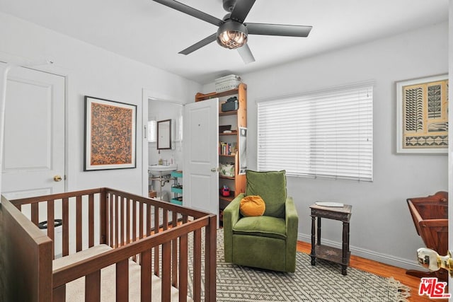 bedroom with a nursery area, ceiling fan, and light hardwood / wood-style floors