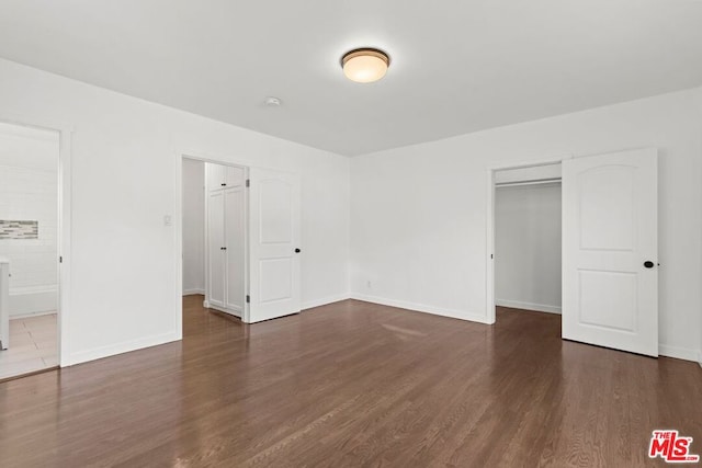 unfurnished bedroom featuring ensuite bathroom, dark hardwood / wood-style flooring, and a closet