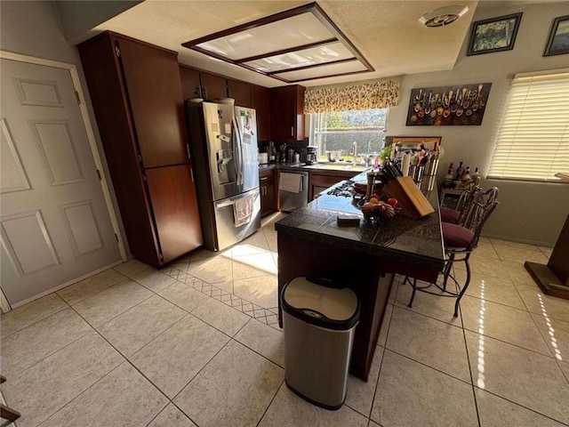 kitchen with sink, light tile patterned floors, appliances with stainless steel finishes, a center island, and a kitchen bar