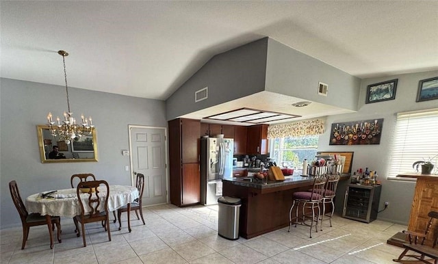 kitchen with vaulted ceiling, light tile patterned floors, stainless steel refrigerator, kitchen peninsula, and a notable chandelier