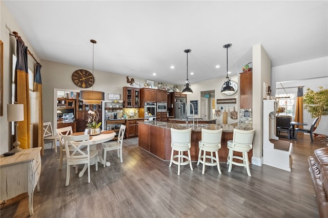 kitchen featuring pendant lighting, a breakfast bar, appliances with stainless steel finishes, dark hardwood / wood-style flooring, and dark stone counters