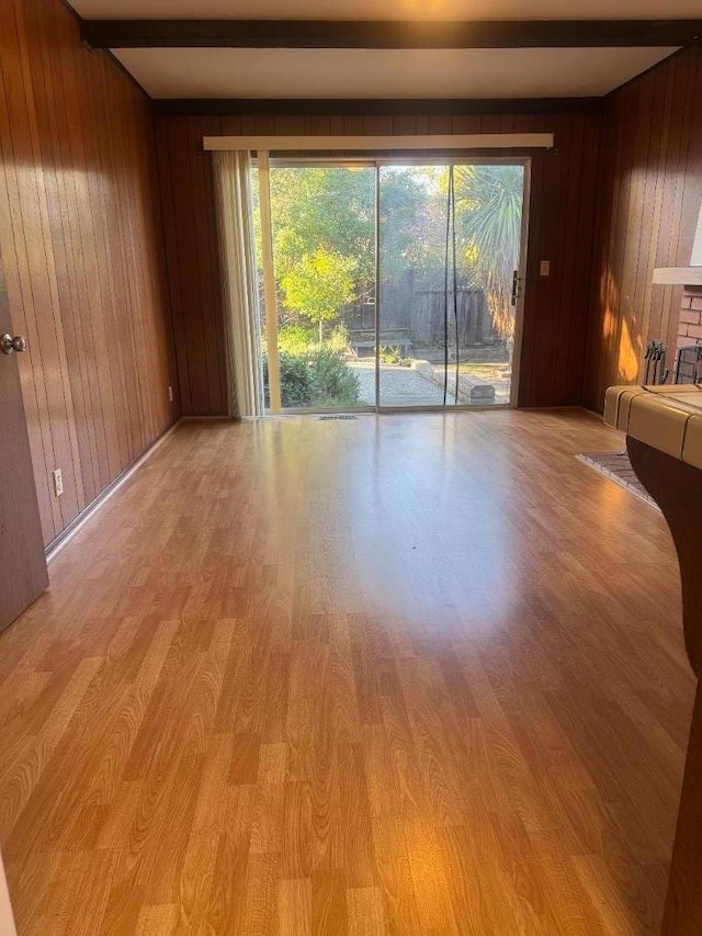 spare room with beam ceiling, light hardwood / wood-style flooring, and wooden walls