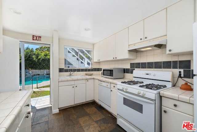 kitchen with white cabinetry, white appliances, tile counters, and backsplash