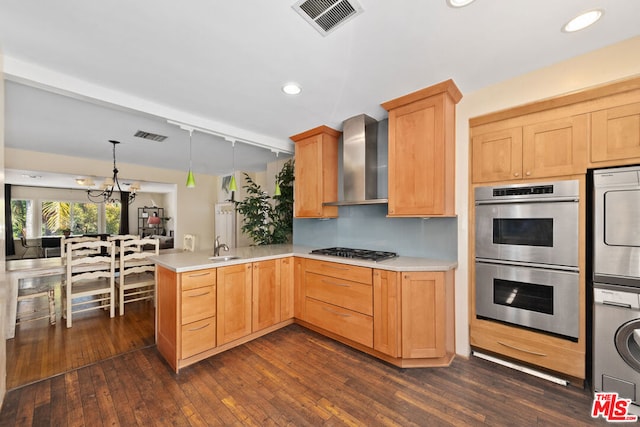 kitchen featuring pendant lighting, sink, appliances with stainless steel finishes, kitchen peninsula, and wall chimney exhaust hood