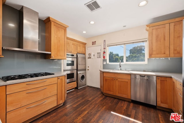 kitchen with appliances with stainless steel finishes, dark hardwood / wood-style floors, sink, stacked washer and dryer, and wall chimney exhaust hood