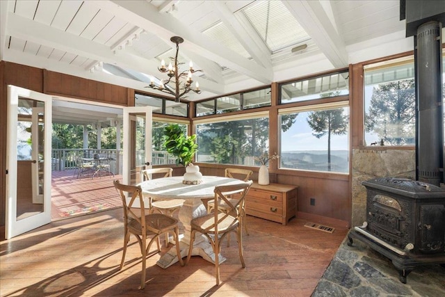 sunroom / solarium with a notable chandelier, beam ceiling, and a wood stove