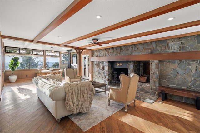 living room featuring wood-type flooring, beam ceiling, and a stone fireplace