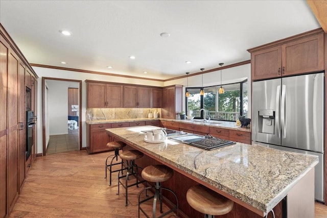 kitchen featuring hanging light fixtures, a center island, light stone counters, black appliances, and light wood-type flooring