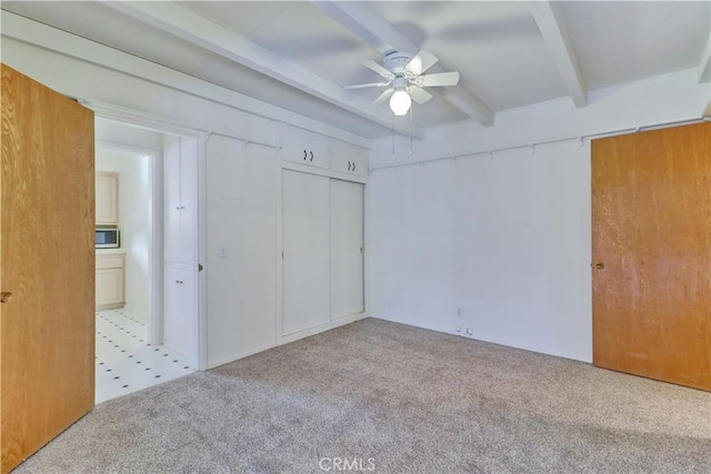 unfurnished bedroom featuring beamed ceiling, ceiling fan, light colored carpet, and a closet