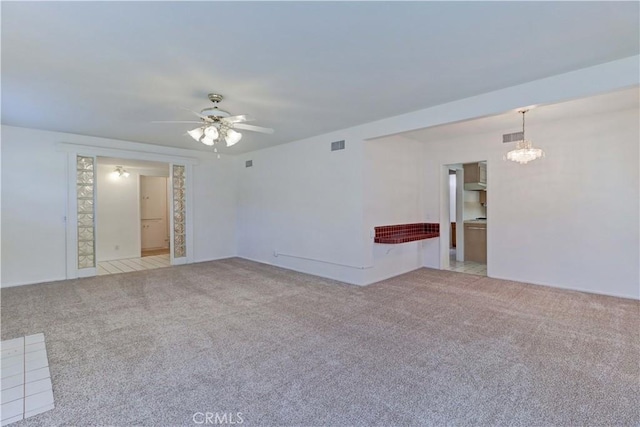 carpeted spare room featuring ceiling fan with notable chandelier