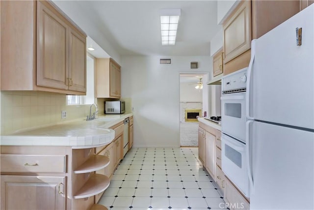 kitchen featuring tasteful backsplash, sink, tile counters, light brown cabinets, and white appliances