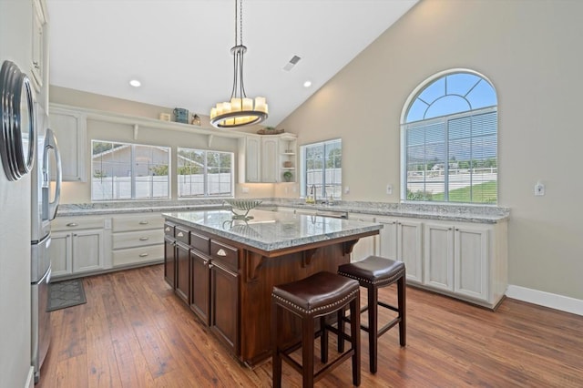 kitchen with dark wood-type flooring, a breakfast bar area, light stone counters, a center island, and stainless steel fridge