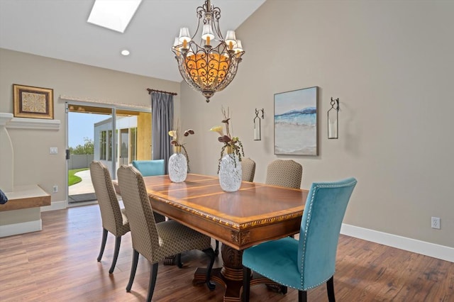 dining room with hardwood / wood-style flooring, lofted ceiling with skylight, and a chandelier