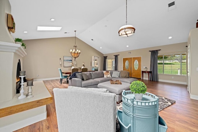 living room featuring an inviting chandelier, vaulted ceiling with skylight, and hardwood / wood-style floors