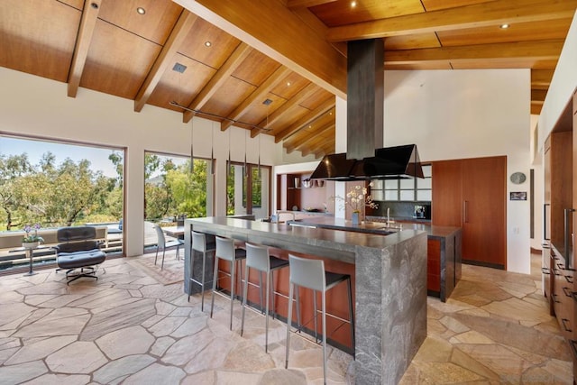 kitchen with a breakfast bar area, hanging light fixtures, high vaulted ceiling, a large island with sink, and beamed ceiling