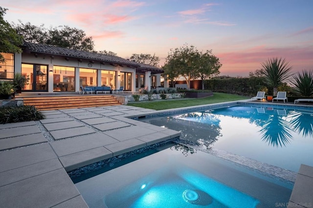 pool at dusk featuring a jacuzzi and a patio