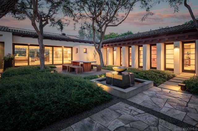 back house at dusk featuring a patio area