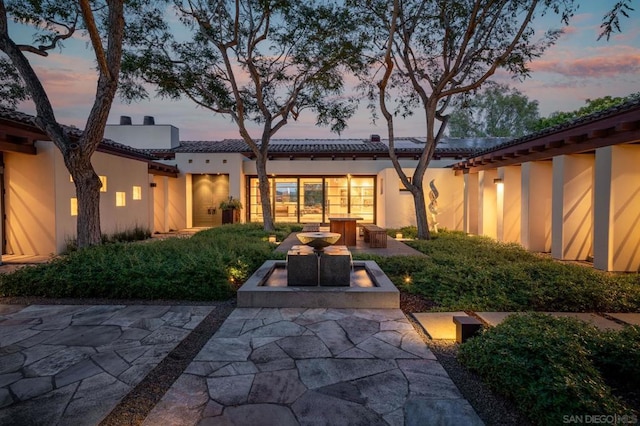 back house at dusk featuring a patio