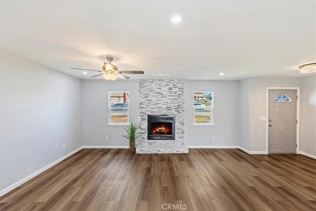 unfurnished living room with a large fireplace, ceiling fan, and dark hardwood / wood-style flooring