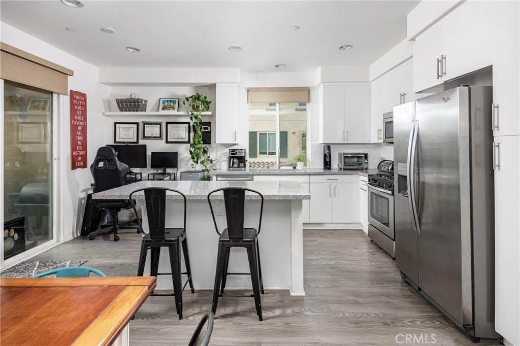 kitchen with a breakfast bar, white cabinetry, stainless steel appliances, light stone countertops, and light wood-type flooring