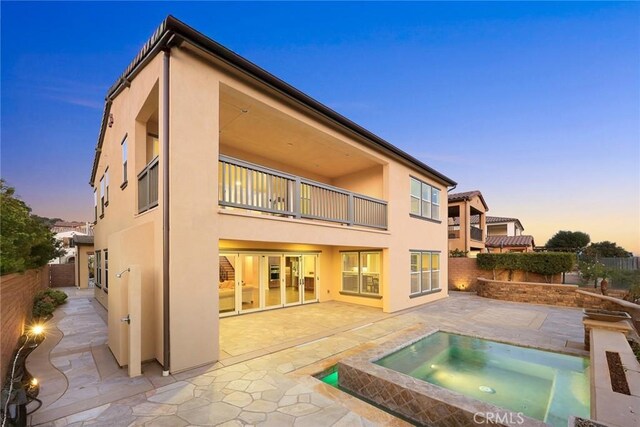 back house at dusk featuring an in ground hot tub and a patio