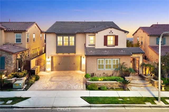 view of front of home featuring a garage, decorative driveway, brick siding, and stucco siding