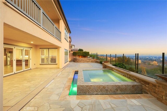 pool at dusk with an in ground hot tub and a patio area