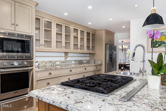 kitchen featuring appliances with stainless steel finishes, pendant lighting, sink, a notable chandelier, and cream cabinetry