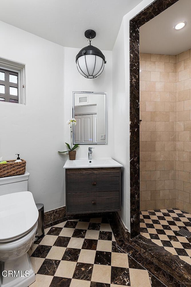 bathroom featuring a tile shower, vanity, and toilet