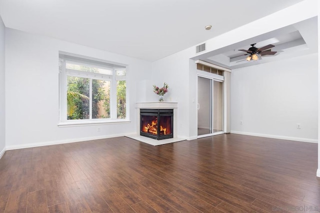 unfurnished living room with ceiling fan, dark hardwood / wood-style flooring, and a tray ceiling