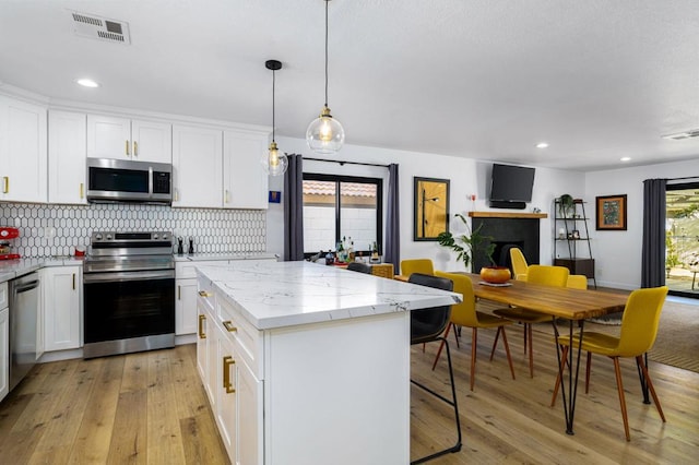 kitchen featuring light hardwood / wood-style flooring, hanging light fixtures, a kitchen island, stainless steel appliances, and white cabinets