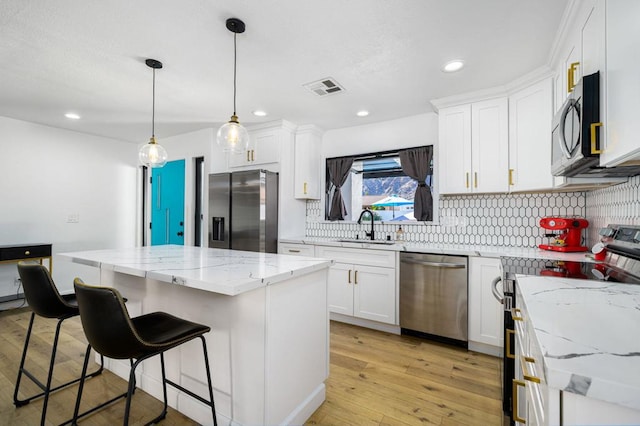 kitchen with white cabinetry, decorative light fixtures, stainless steel appliances, and a center island