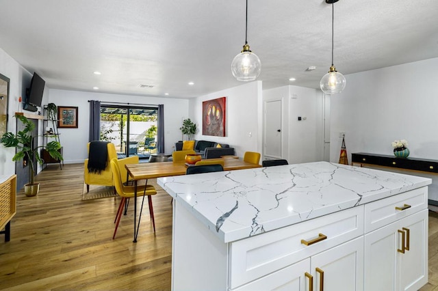 kitchen featuring hanging light fixtures, light stone counters, white cabinets, and light wood-type flooring