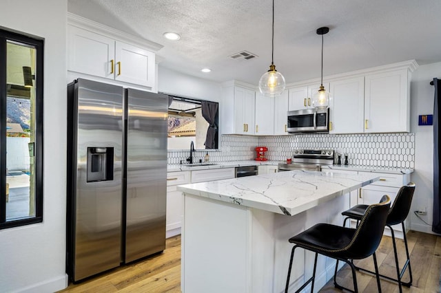 kitchen with decorative light fixtures, a center island, light hardwood / wood-style flooring, stainless steel appliances, and white cabinets