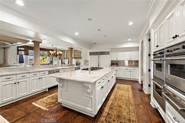 kitchen with appliances with stainless steel finishes, white cabinetry, decorative columns, a center island, and tasteful backsplash